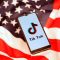 Tik Tok logo is displayed on the smartphone while standing on the U.S. flag in this illustration